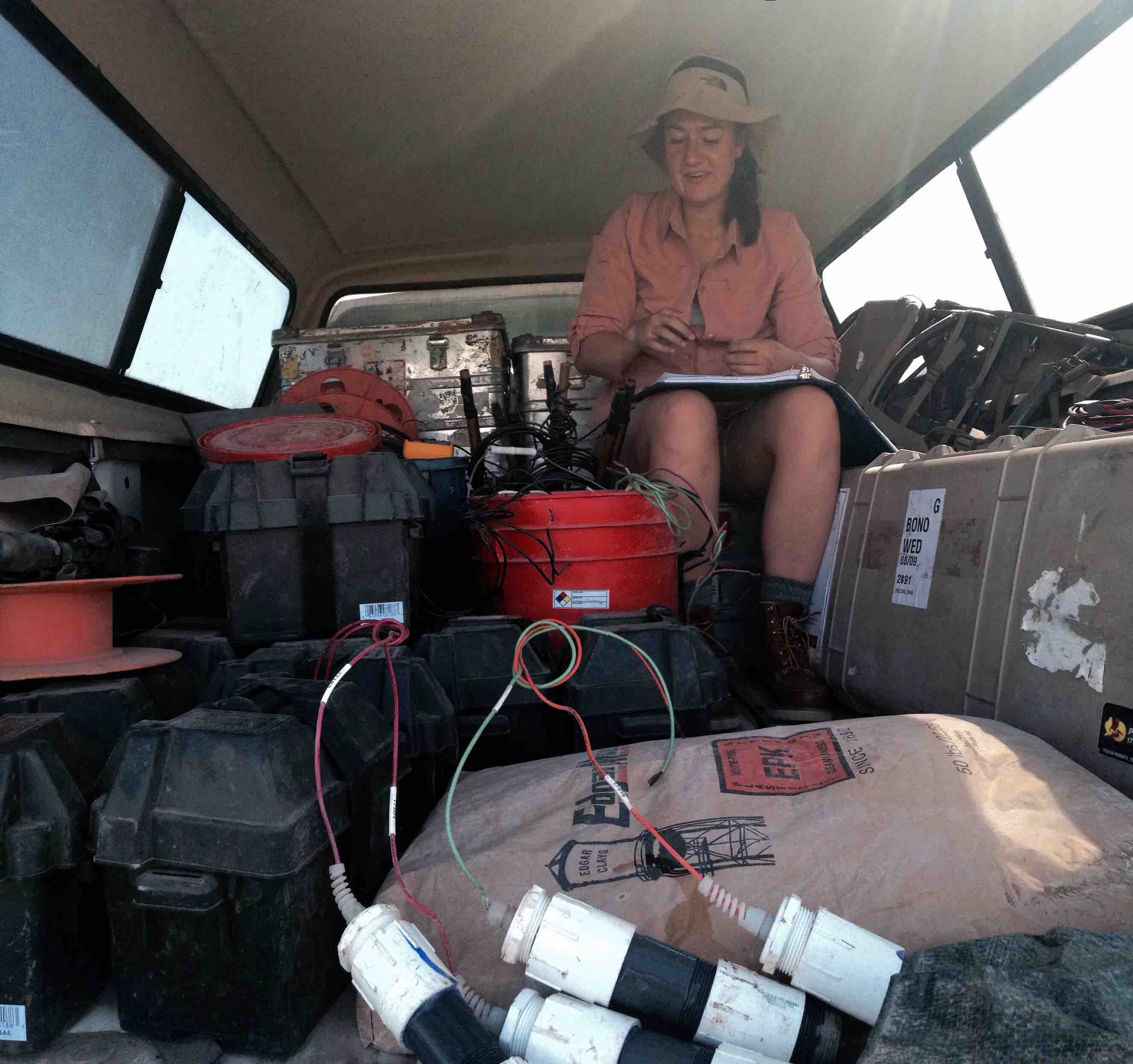 Eva sitting in her work truck on a bunch of experimental gear with a notebook.